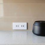 Widok zbliżenia na blat kuchenny z gniazdkiem elektrycznym zamontowanym nad blatem i podstawą małego sprzętu kuchennego po prawej stronie.